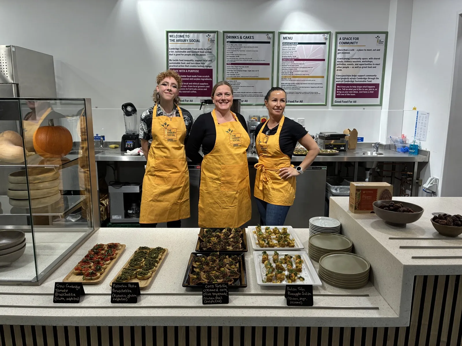 Cambridge Sustainable Food volunteers behind the counter at The Arbury Social on its opening day, with the menu boards behind them